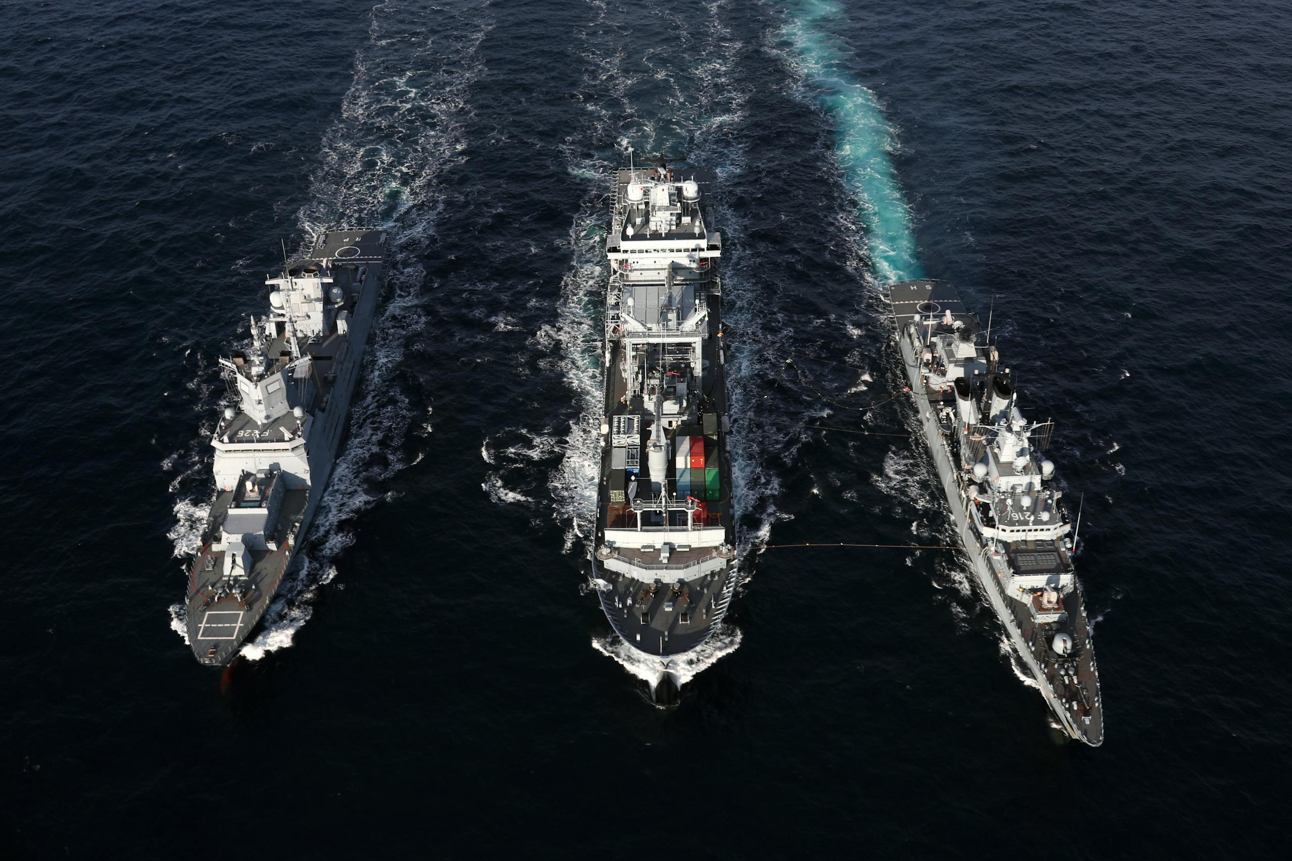 Naval ships sailing in formation on open sea, aerial view highlights naval coordination and strategy.